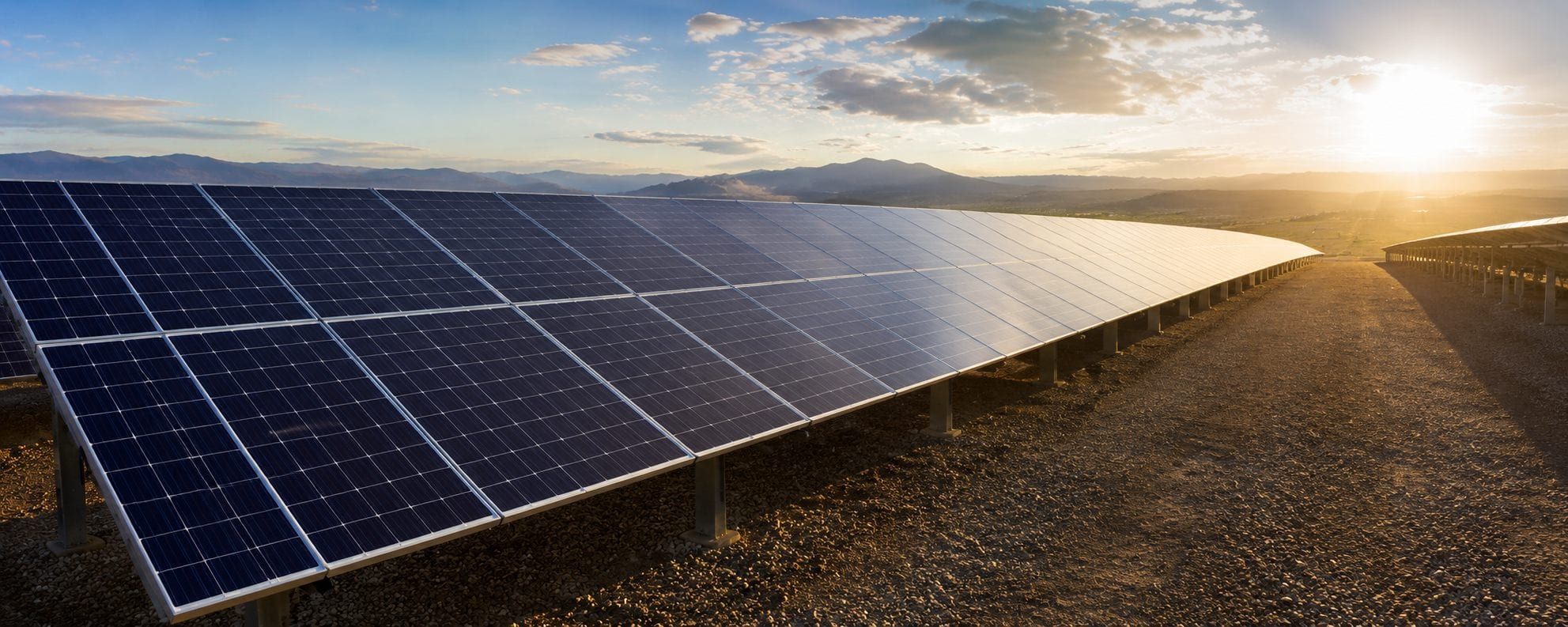 Campo solar industrial con montañas y luz de atardecer